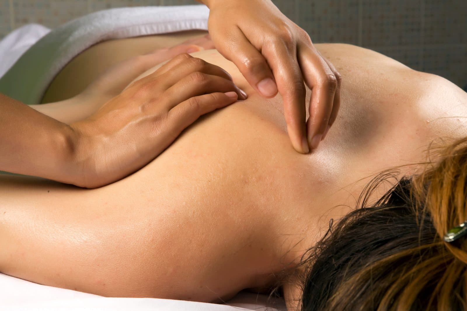 Hands working the upper back and shoulder blade of a patient lying face down on the table.