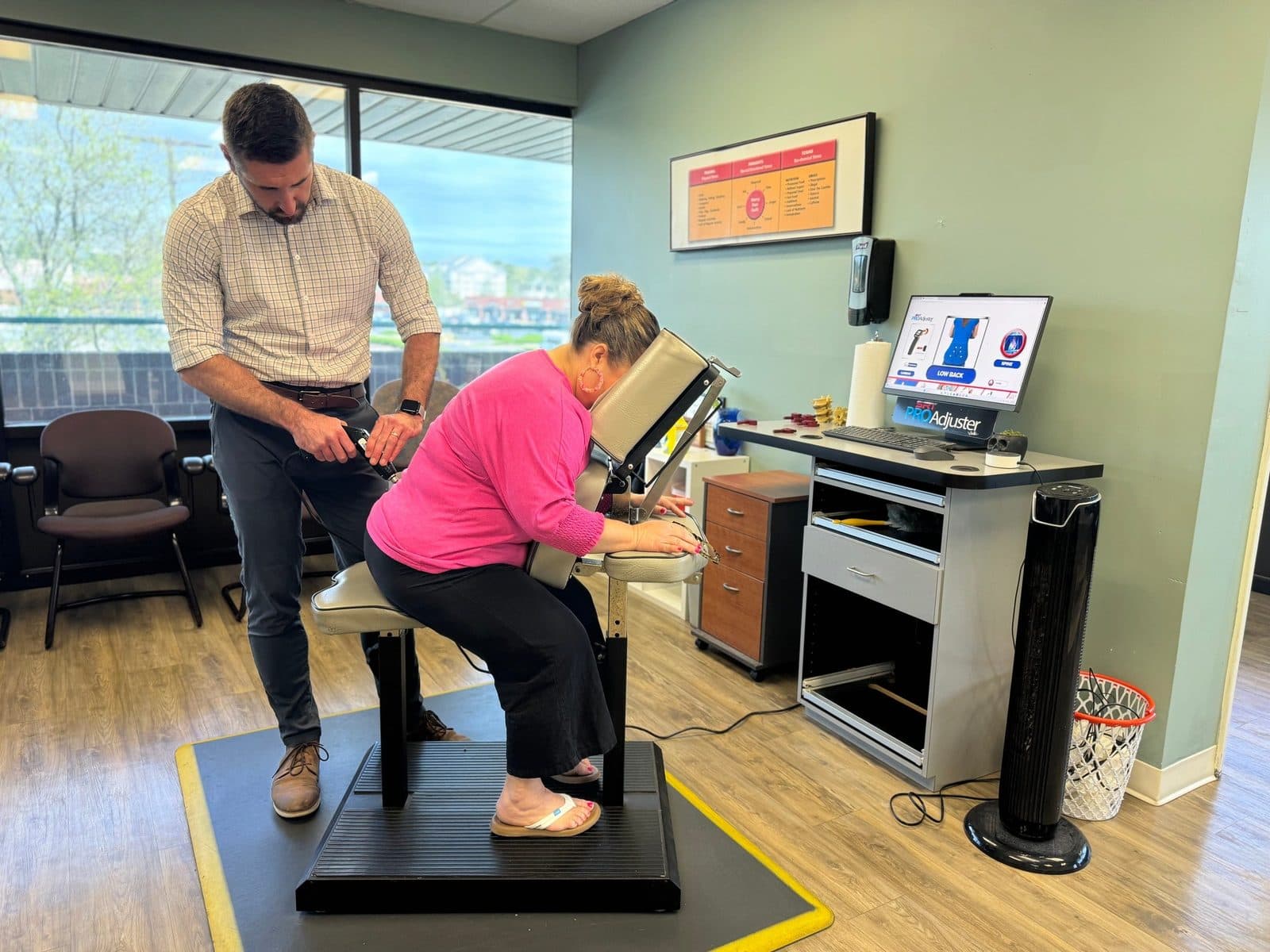 Dr. Paul using the ProAdjuster instrument on a patient seated in the treatment chair, with the Sigma ProAdjuster screen beside them.